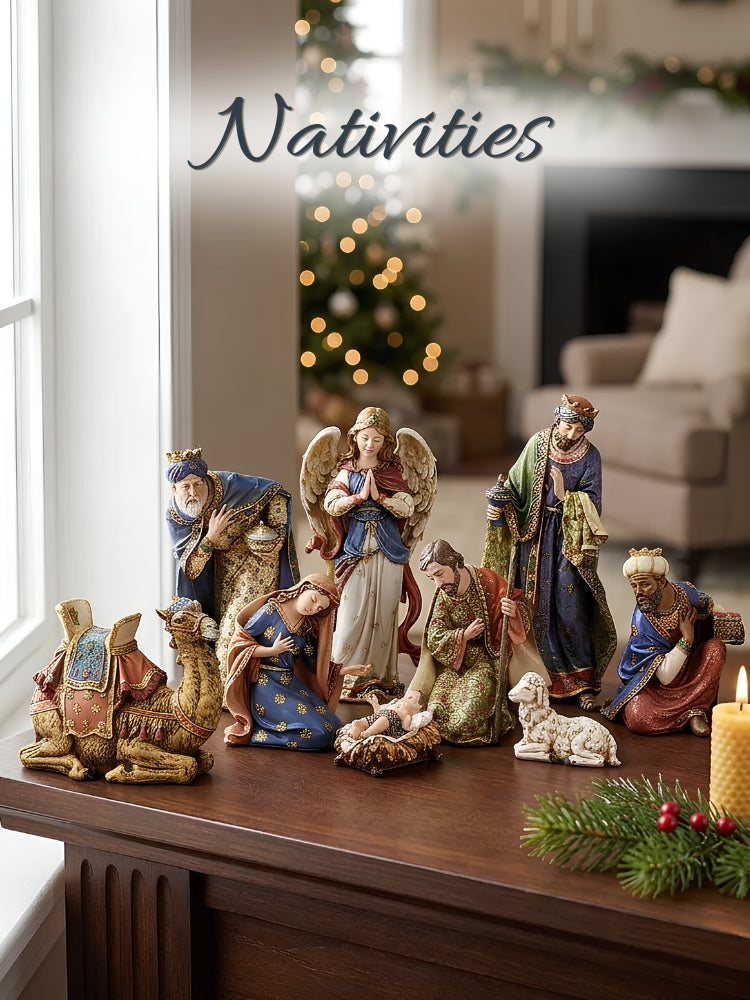 A ceramic Nativity set displayed on a wooden table in a cozy living room setting with a blurred Christmas tree in the background. The set includes figurines of the three wise men, a camel, Mary, Joseph, baby Jesus, an angel, and a sheep, with a lit candle and pine branch in the foreground.