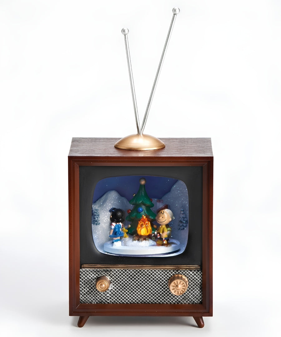A retro-style wooden television figurine with two metal antenna rods, featuring a snow globe display inside the screen with Peanuts characters, a Christmas tree, and a campfire.