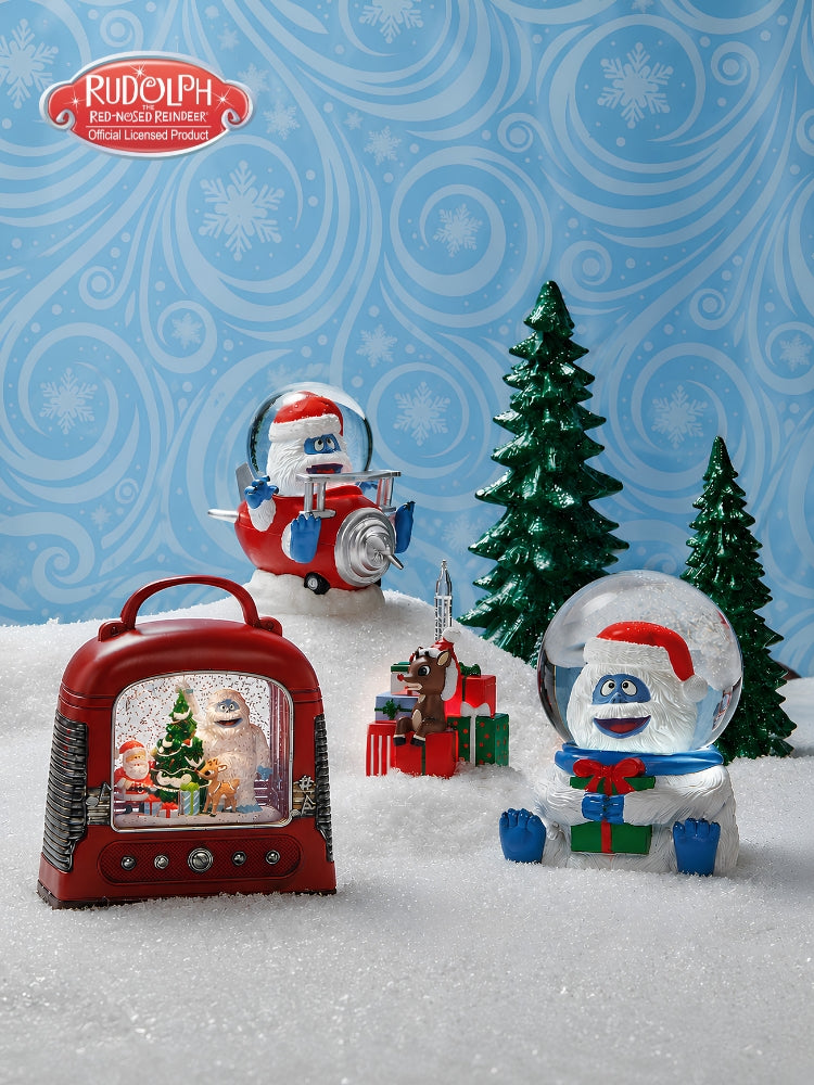 Rudolph the Red-Nosed Christmas Ornament set featuring a red snow globe radio, a red snow globe ornament of Rudolph, a red snow globe Santa, and a red snow globe gift box, displayed on a snowy surface against a blue patterned background with green Christmas trees.